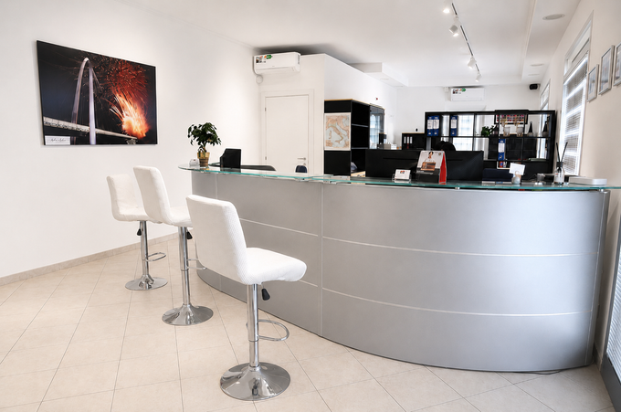 Area reception moderna con scrivania curva color argento, sedie bianche e una foto della città sulla parete.