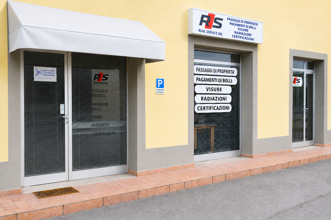 Vetrina con porte e finestre in vetro, tenda da sole bianca e insegna su una facciata esterna di un edificio giallo.