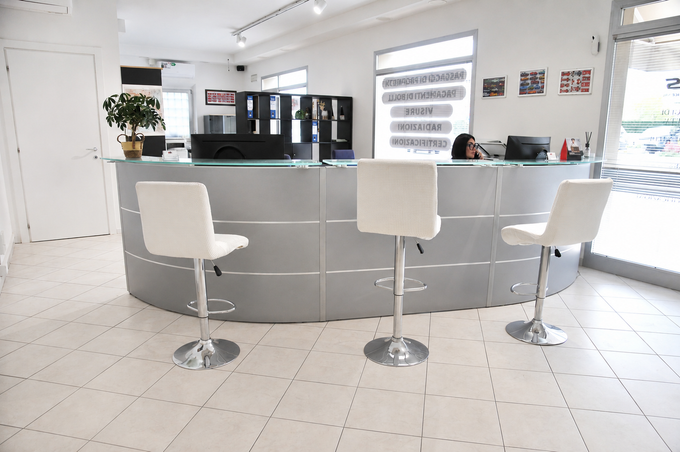 Moderna area reception per ufficio, di colore bianco, con scrivania curva grigia e tre sedie bianche.