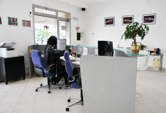 Persona seduta a una scrivania in un ufficio luminoso con computer e sedie.