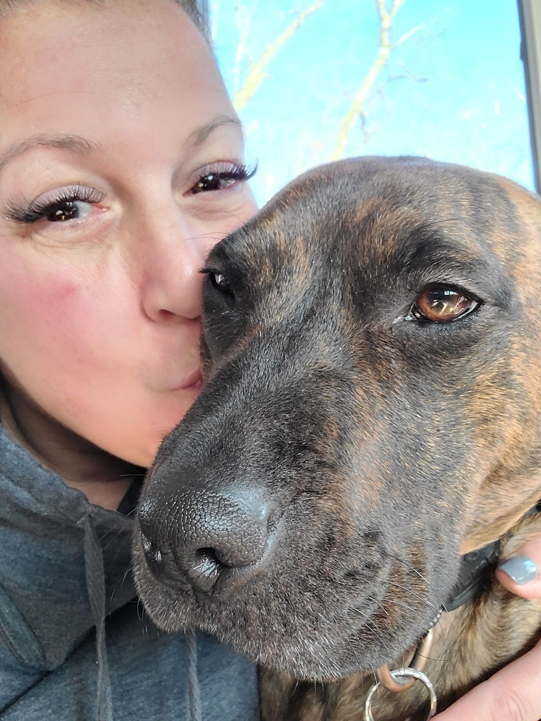 A woman is kissing a dog on the nose.