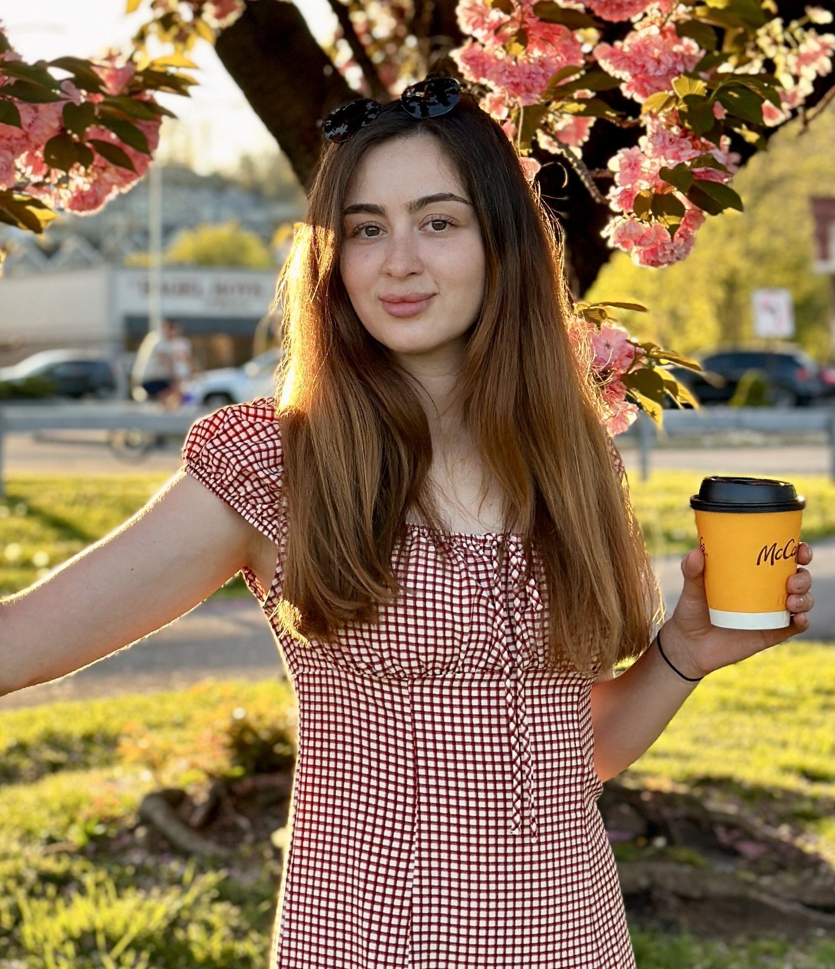 A woman is holding a cup of coffee in front of a cherry blossom tree.