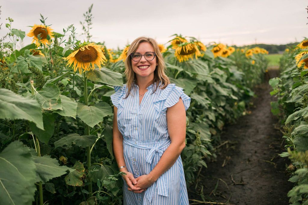 A woman in a blue dress is standing in a field of sunflowers.