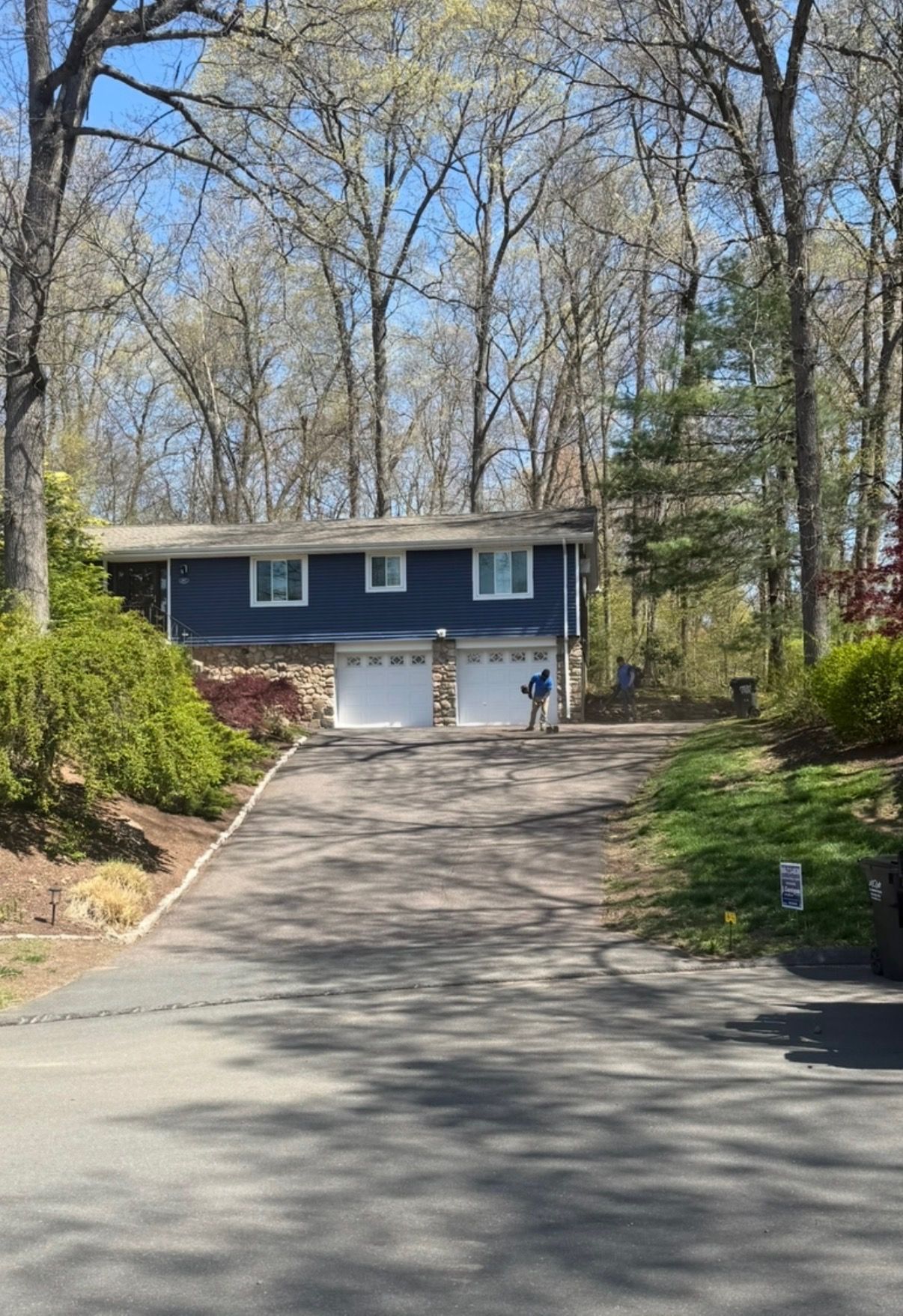Blue house at top of a long driveway, surrounded by trees and shrubs on a sunny day