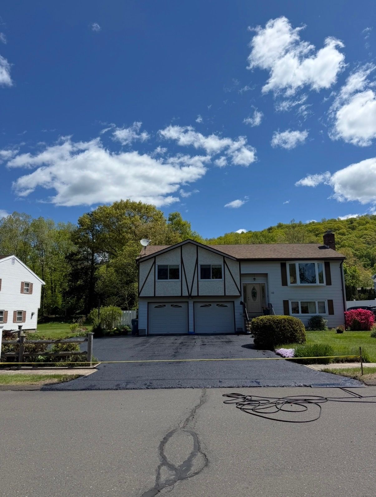 Two-story suburban house with a garage, driveway, and blue sky with clouds over a quiet street