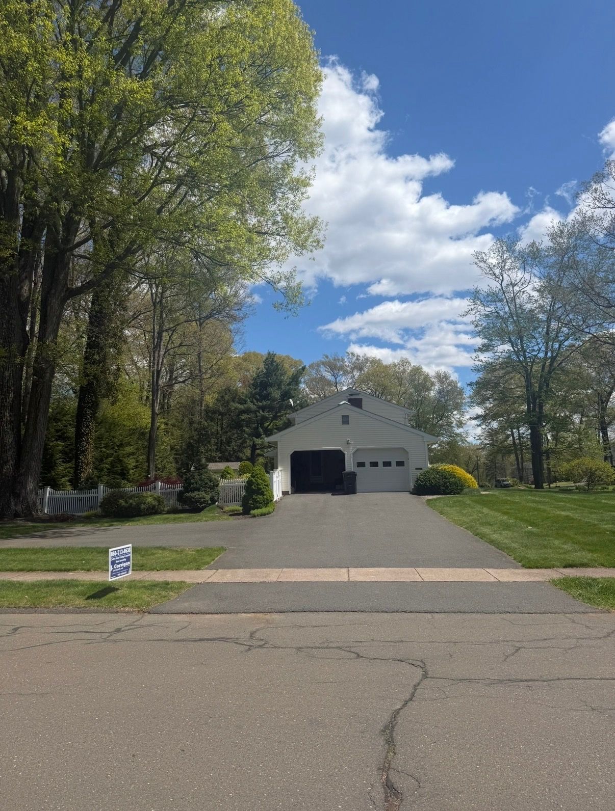 Suburban driveway leading to a white garage under blue sky, lined with trees and grass.