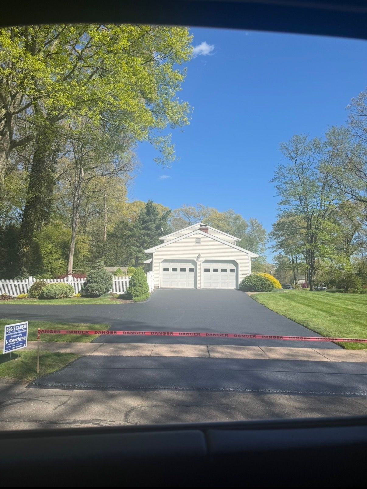 Driveway leading to a white two-story house with a double garage, surrounded by trees and lawn.