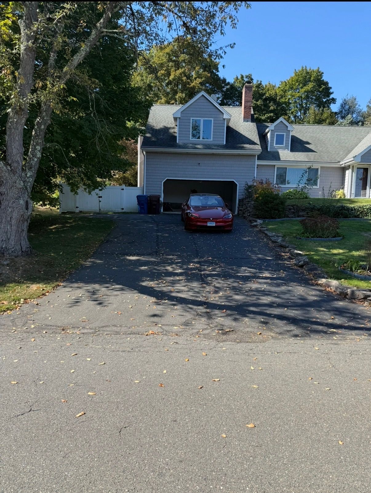 Suburban house with a red car parked in the driveway, framed by trees and a sunny front yard.