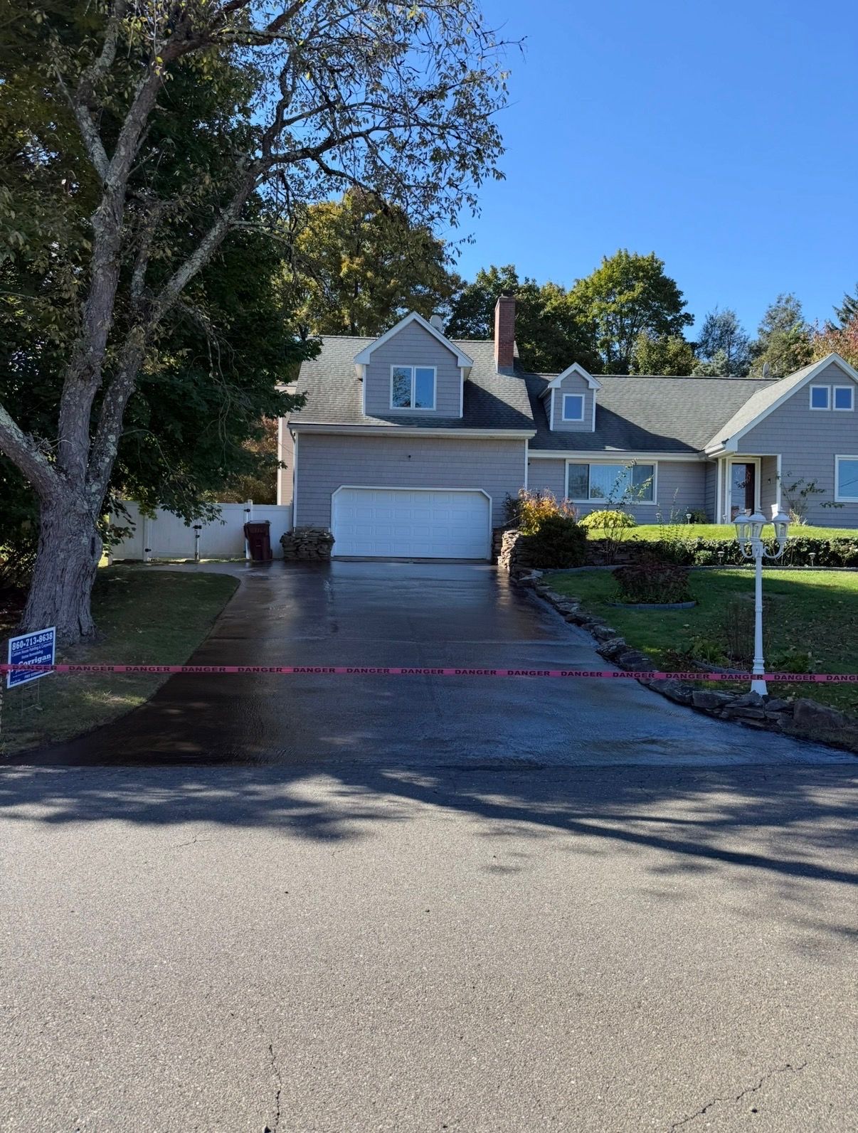 Suburban house with double garage, trees, and red caution tape across the driveway under a blue sky
