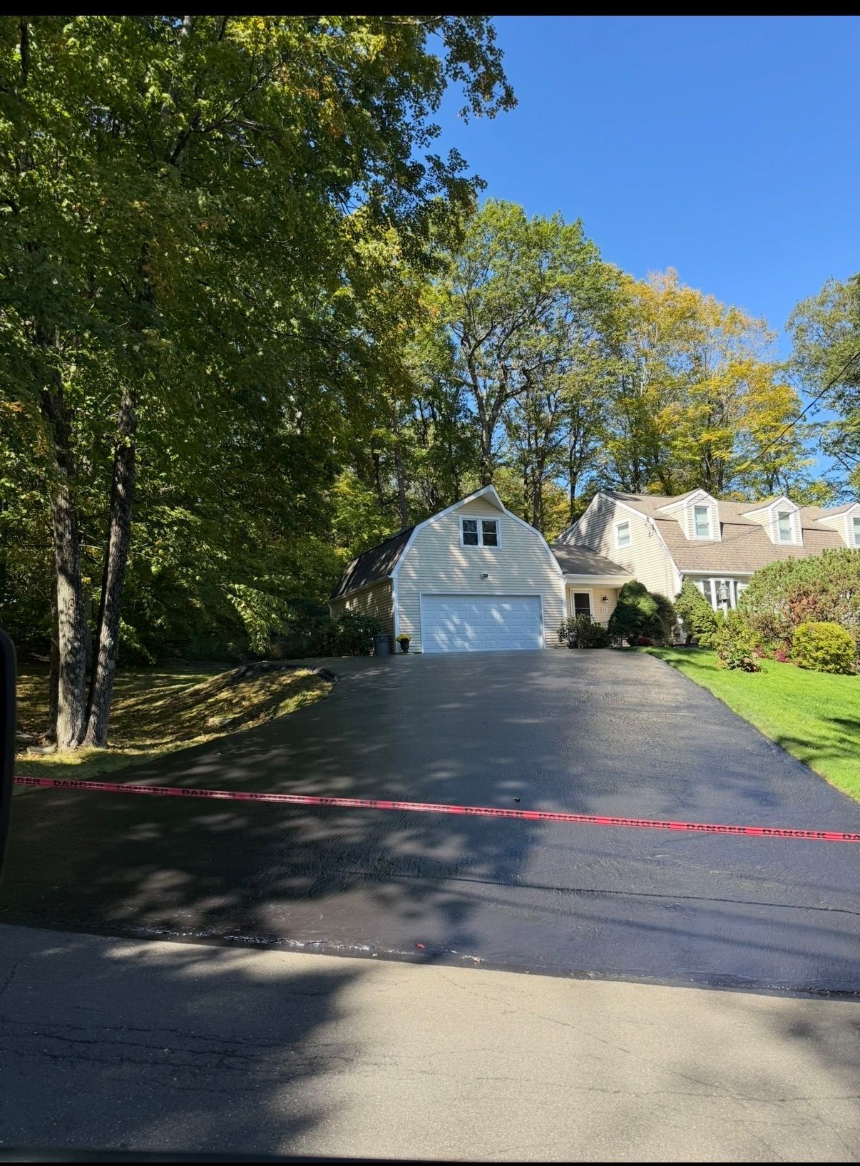 Driveway leading to a white garage on a sunny suburban property, with trees and a red barrier tape across the entrance