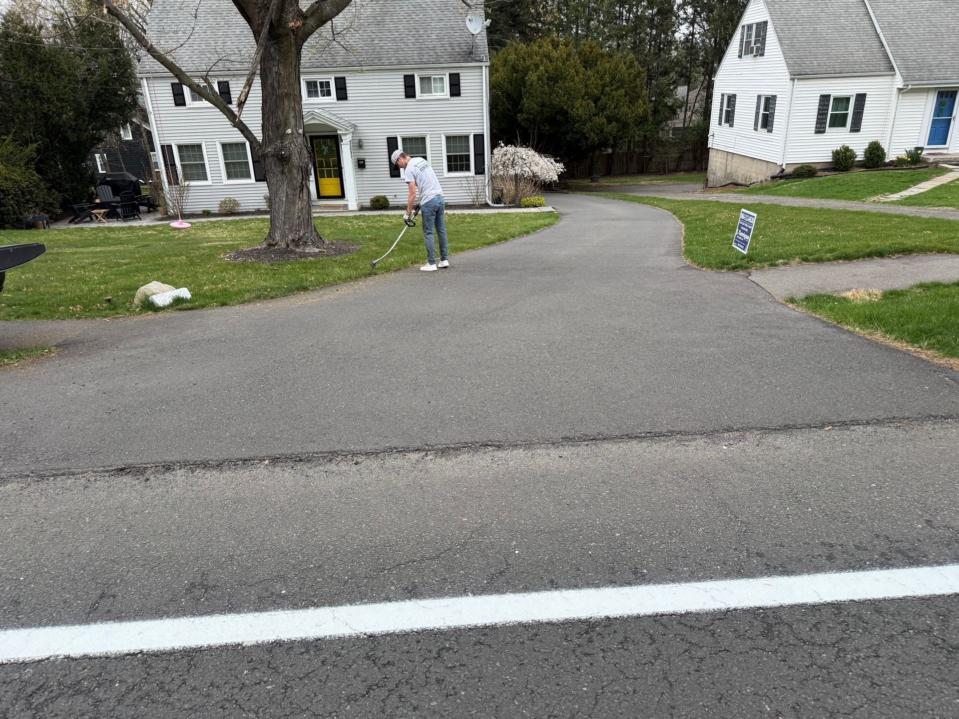 Residential street with a person standing near a driveway between white houses and trees