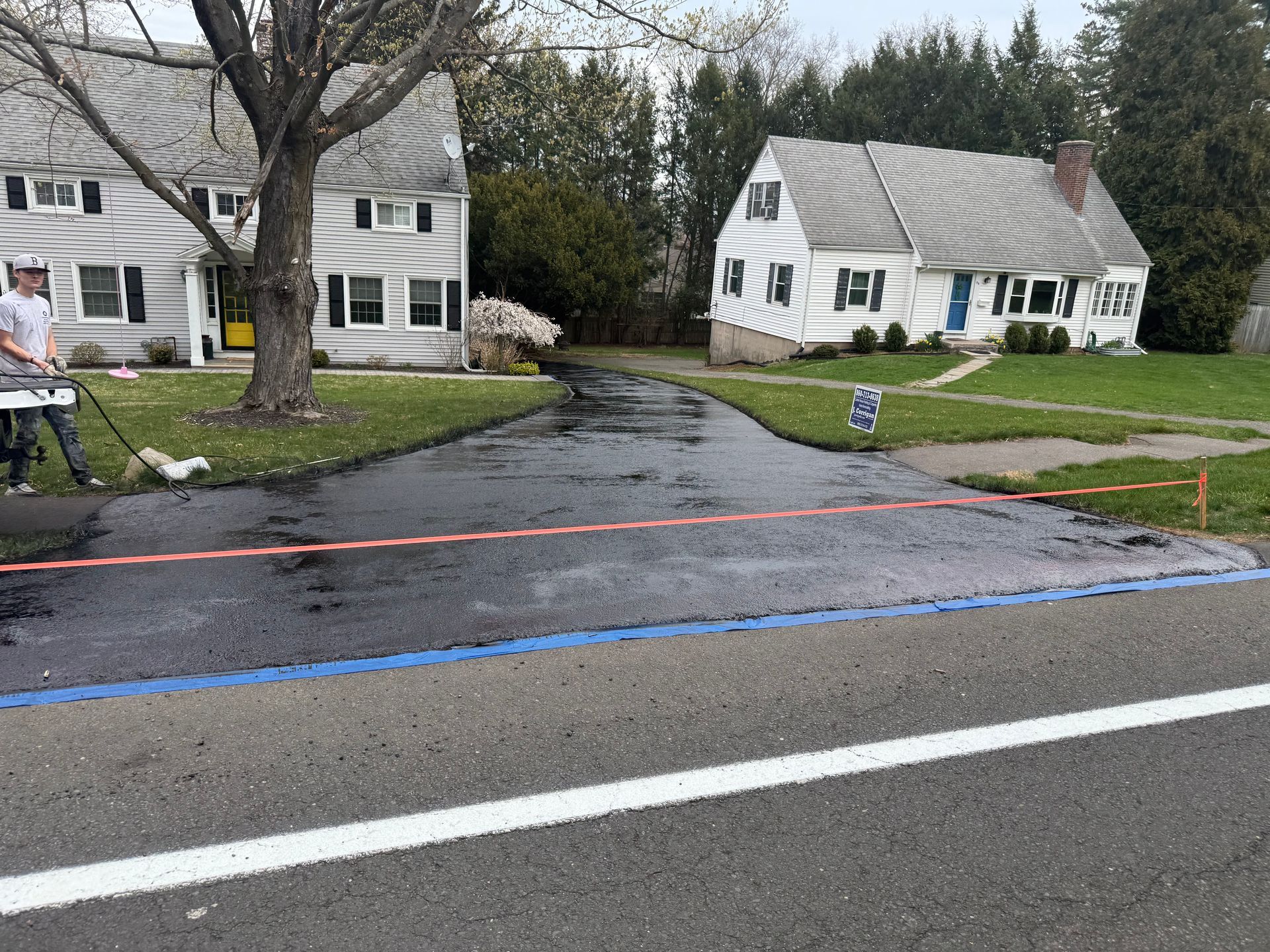 Driveway crossing a wet road in a quiet suburban neighborhood with houses and trees after rain.