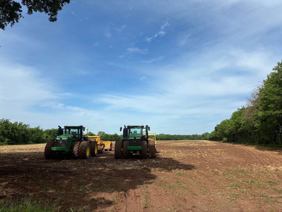 Two green tractors harvesting a brown field under a bright blue sky