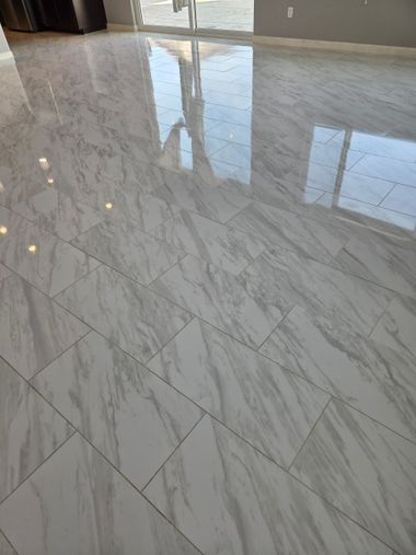 Woman kneels polishing a marble floor in a grand room, holding a cleaning bottle nearby.