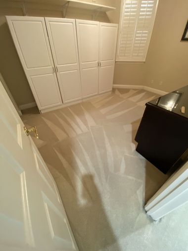 Empty carpeted bedroom with white closets, shuttered window, and dark dresser near the door