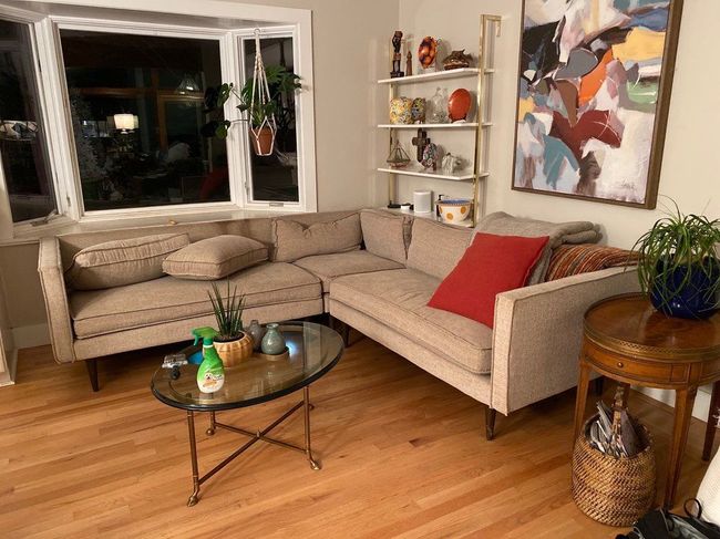 Cozy living room with beige sectional, glass coffee table, wooden floor, window, shelves, and abstract wall art