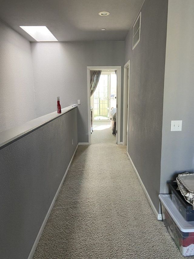 Empty living room with light wood floor and a white fireplace mantel against beige walls.