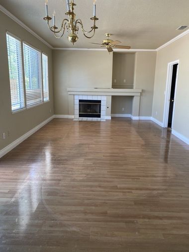 Empty living room with hardwood floors, fireplace, ceiling fan, chandelier, and large windows on the left