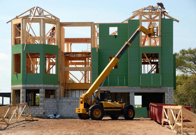 Construction of a two-story house, using a forklift to hoist materials. Green sheeting covers wooden frame.