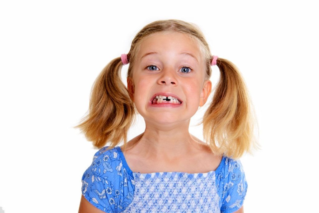 Child making a goofy face, smiling with pigtails and a blue dress on a white background