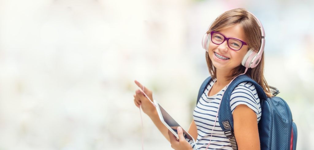 Smiling student with backpack holding a tablet outdoors on a bright day