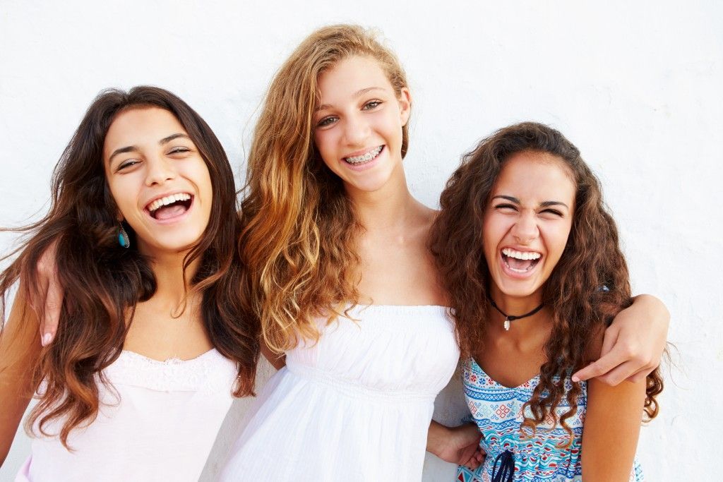 Three smiling women standing close together in white and colorful tops, laughing against a bright white background