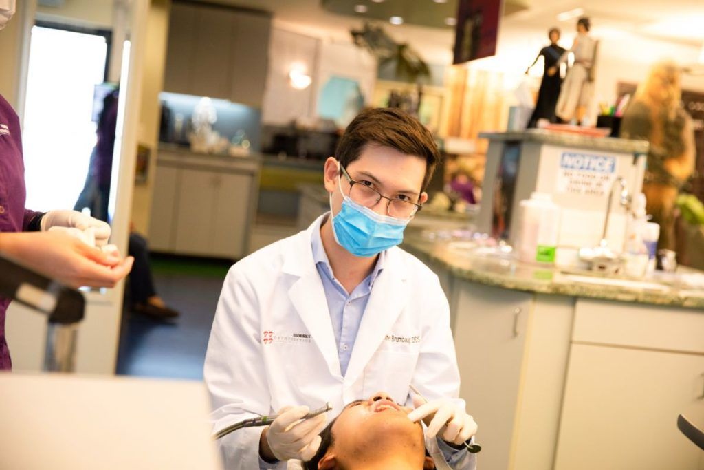Dentist wearing a blue mask examines a patient in a clinic