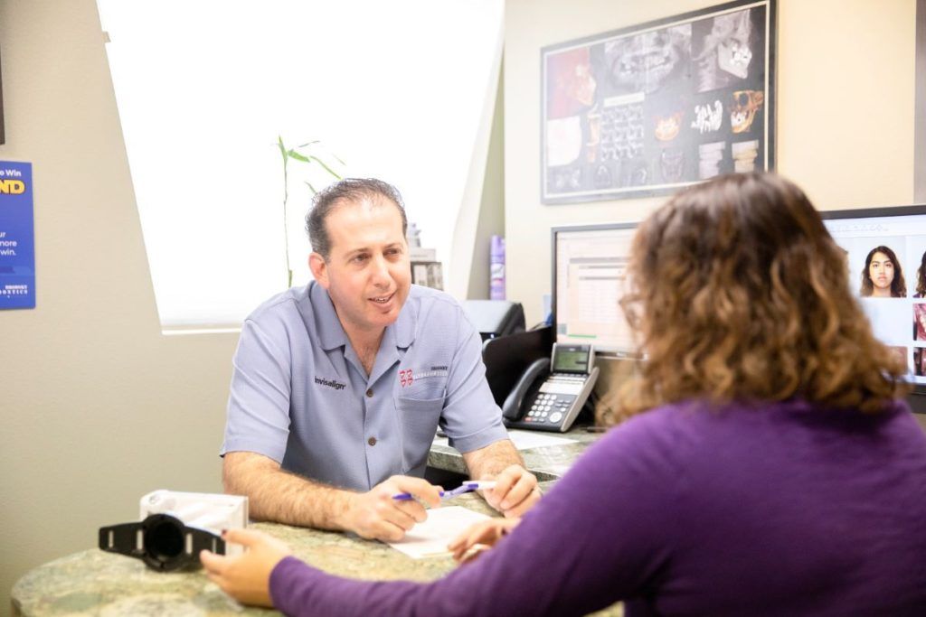 Two people talking across a desk in an office, with paperwork and a phone nearby.