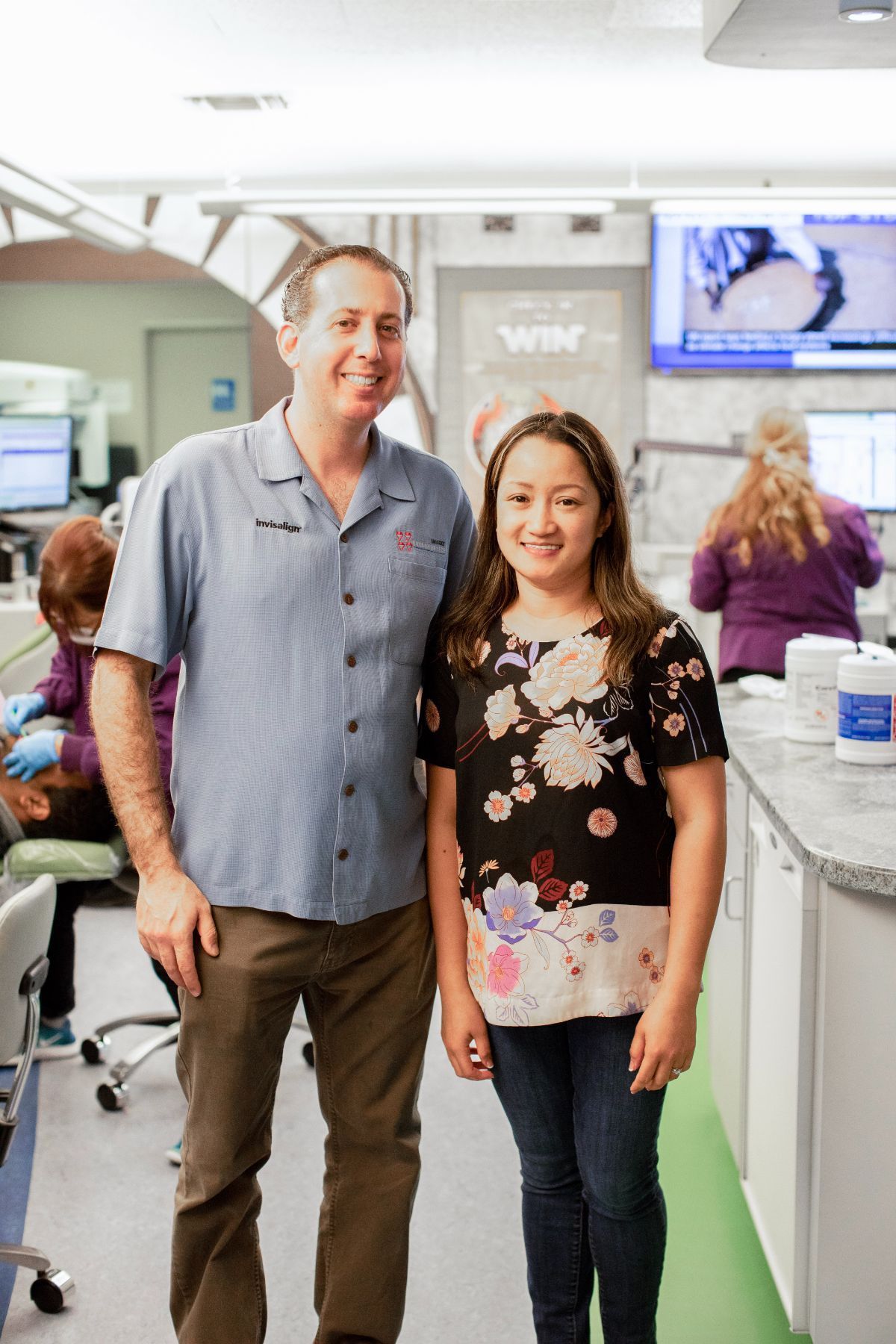 Two people standing in a bright hospital hallway, smiling at the camera.
