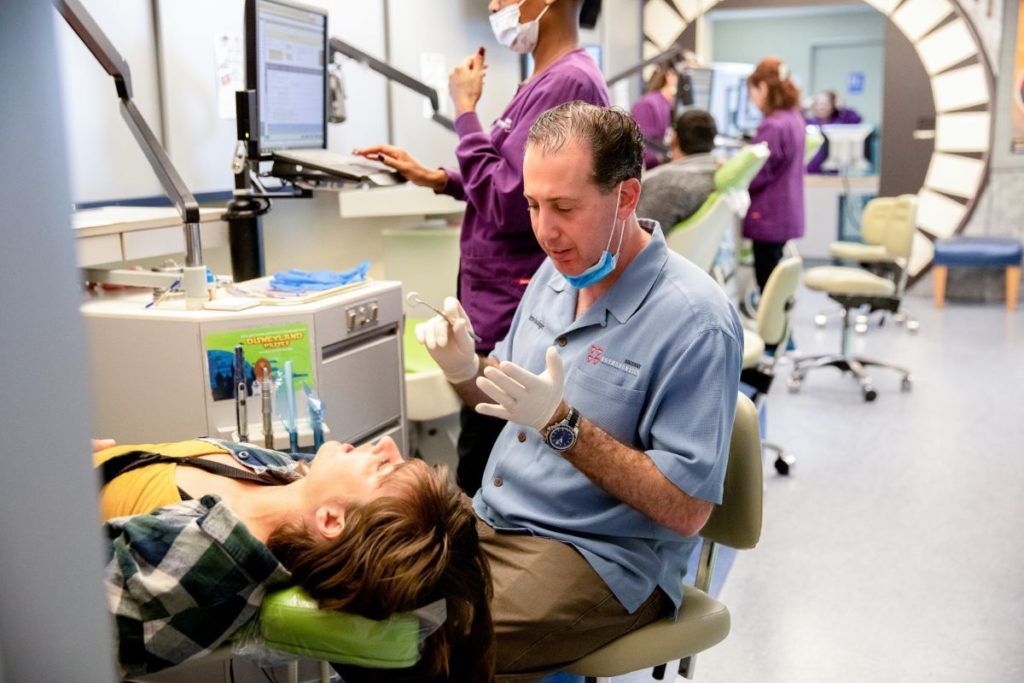 Dental clinic with a patient in a chair and a dentist working beside them under bright lights