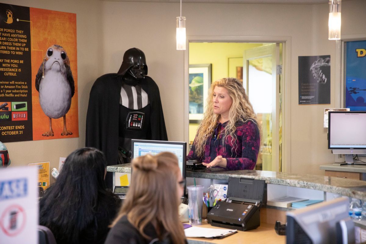 Woman at a counter facing Darth Vader and a large bird poster in an office lobby.
