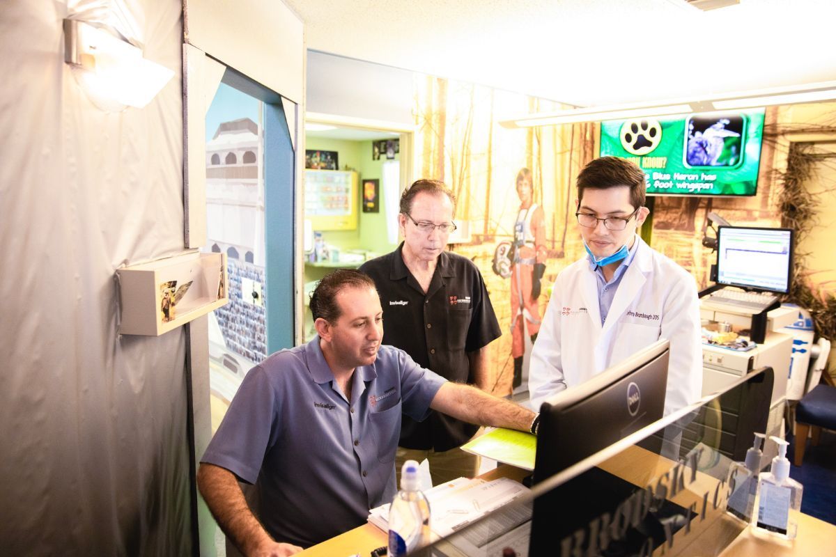 Three people working at a computer in a bright office, with monitors and medical equipment nearby