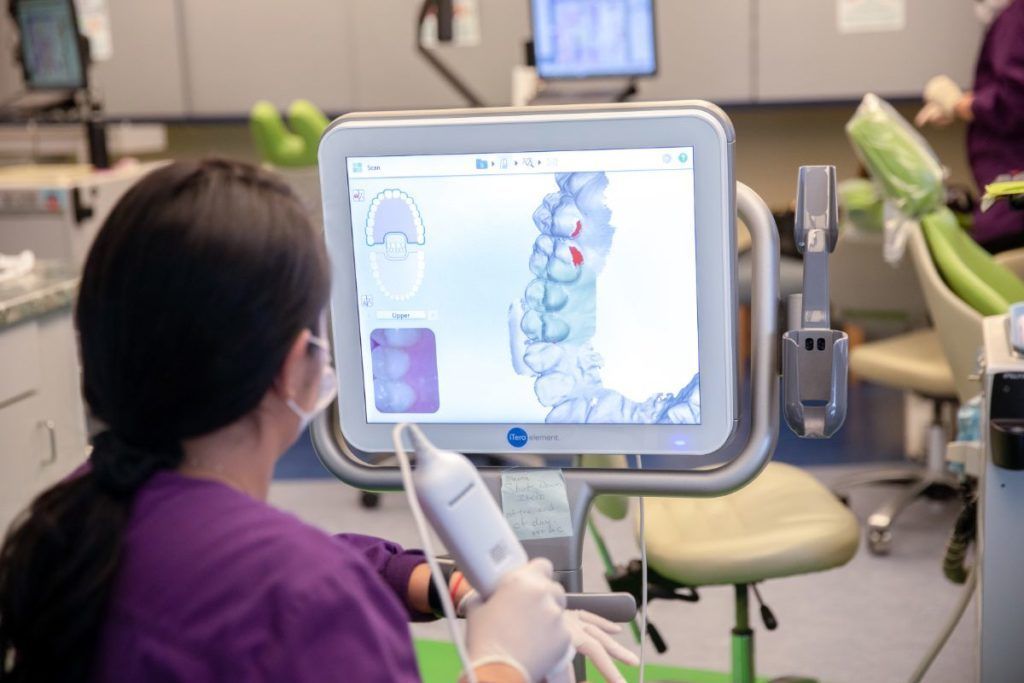Person using a tablet controls a spine model in a dental clinic, with green exam chairs in the background