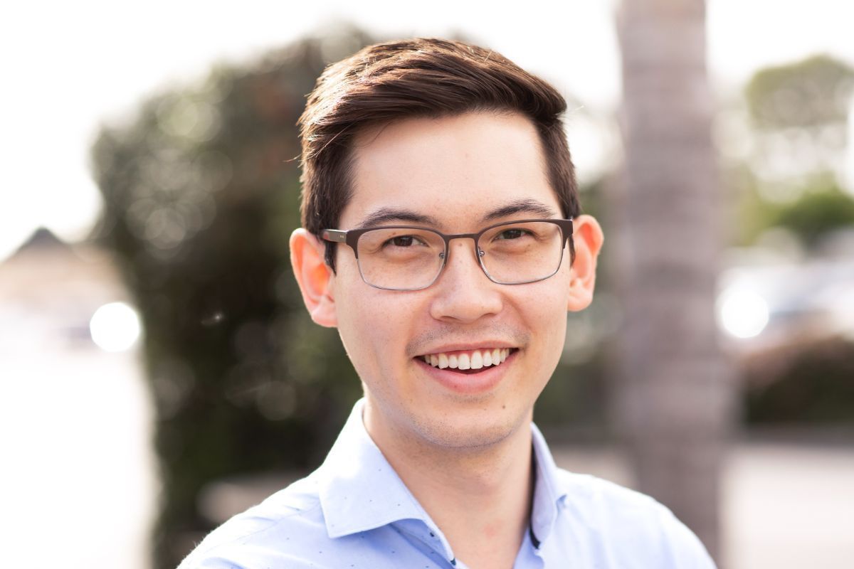 Smiling man with glasses in a light blue shirt outdoors in soft sunlight