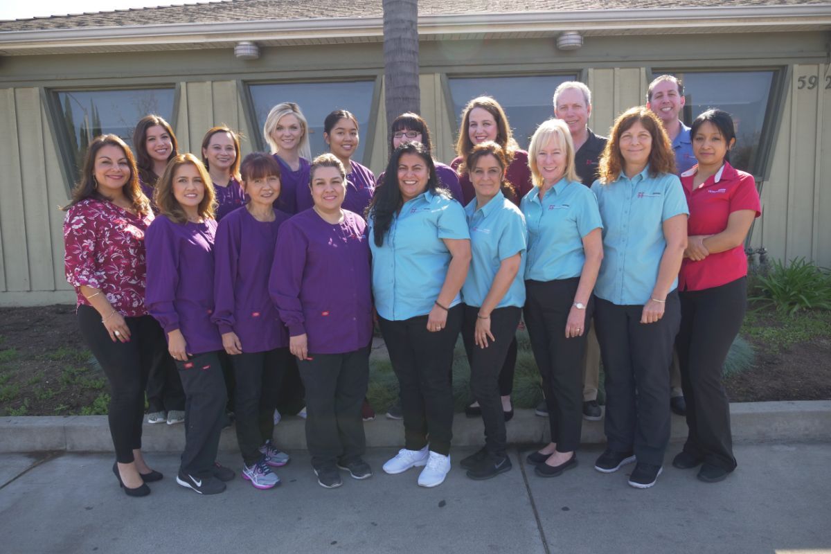 Group of people posing outdoors in front of a building, several wearing purple and teal shirts.