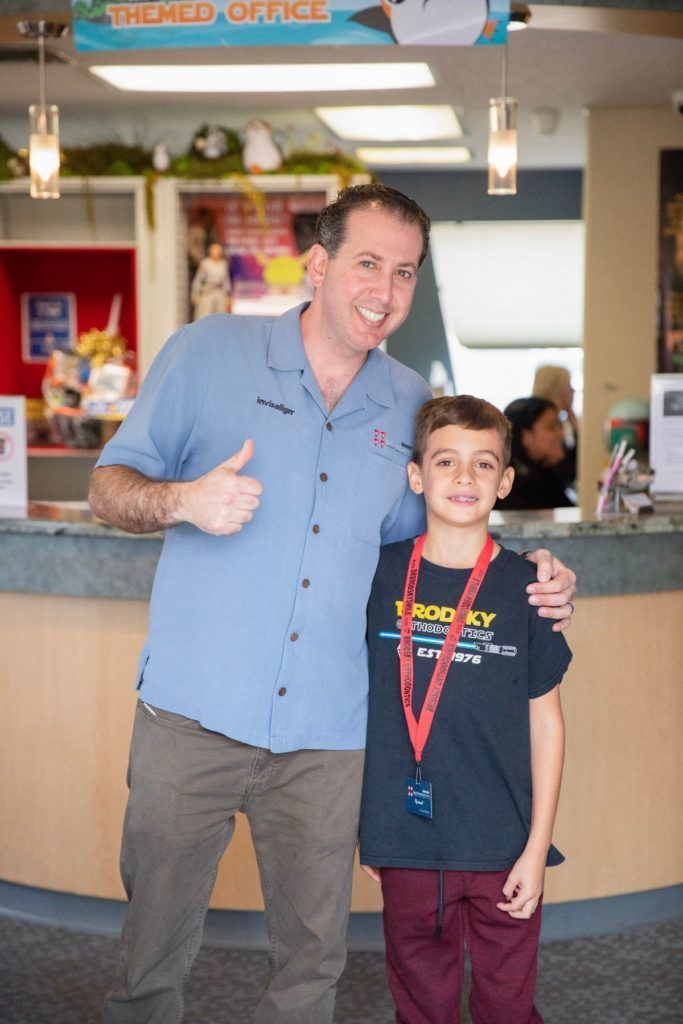 Two people posing indoors at a counter, smiling and giving thumbs up.