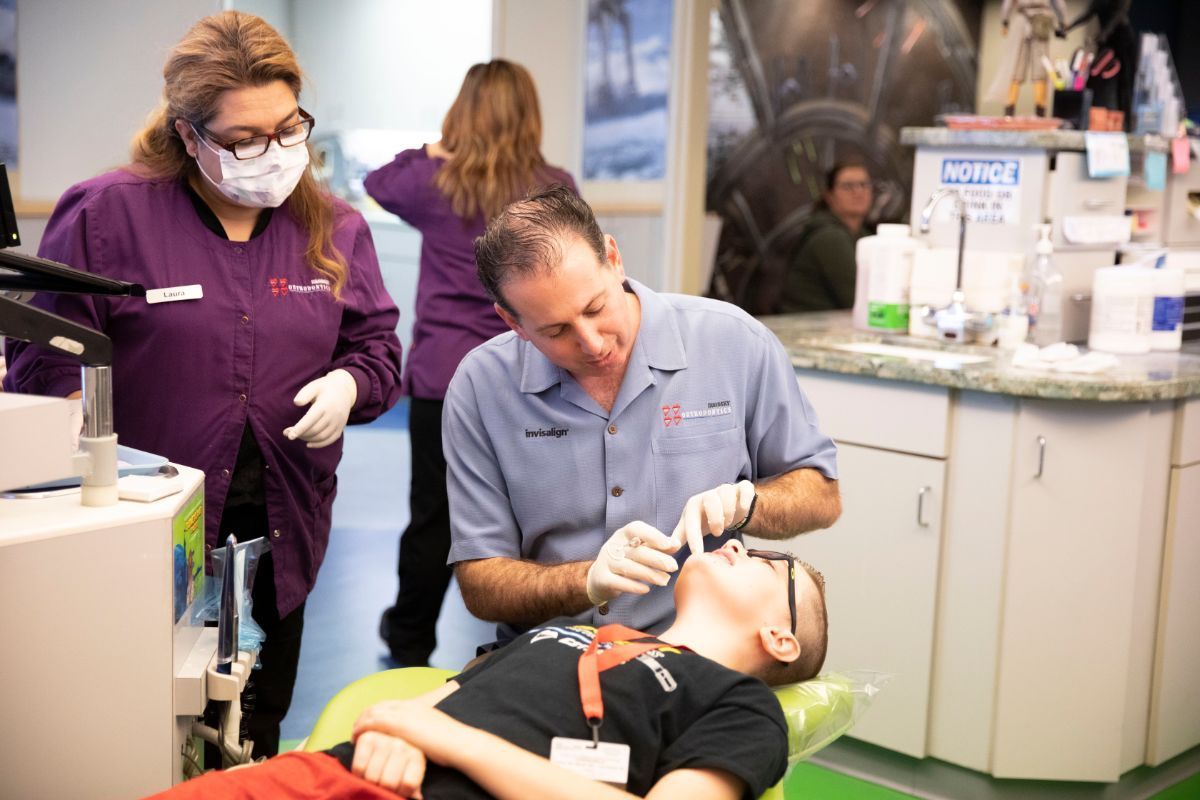 Dentist treating a patient while a masked assistant observes in a clinic setting