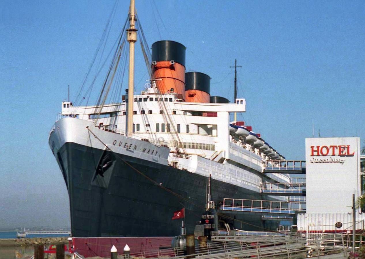 Large ocean liner docked beside a hotel building under a clear blue sky