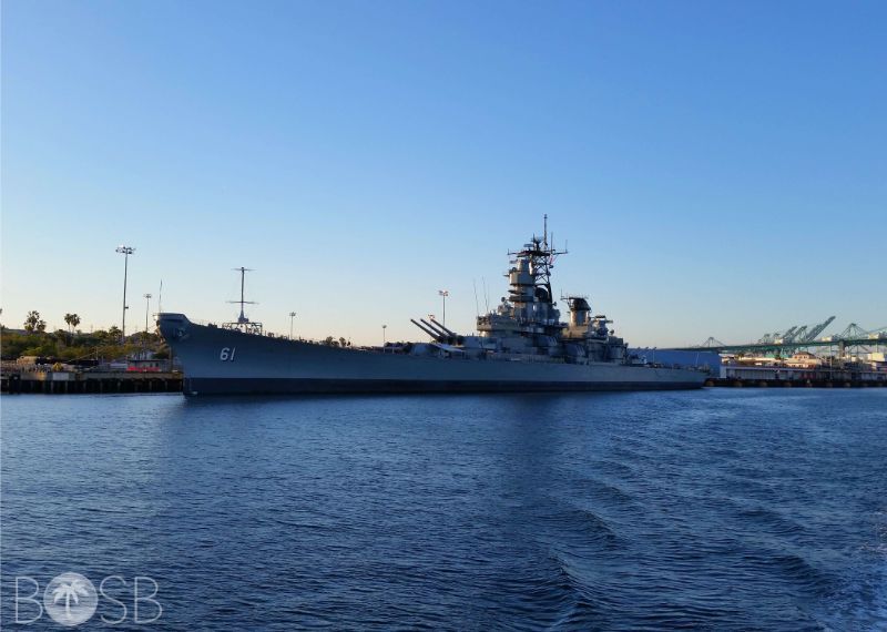 Gray naval warship docked in a harbor under a clear blue sky.
