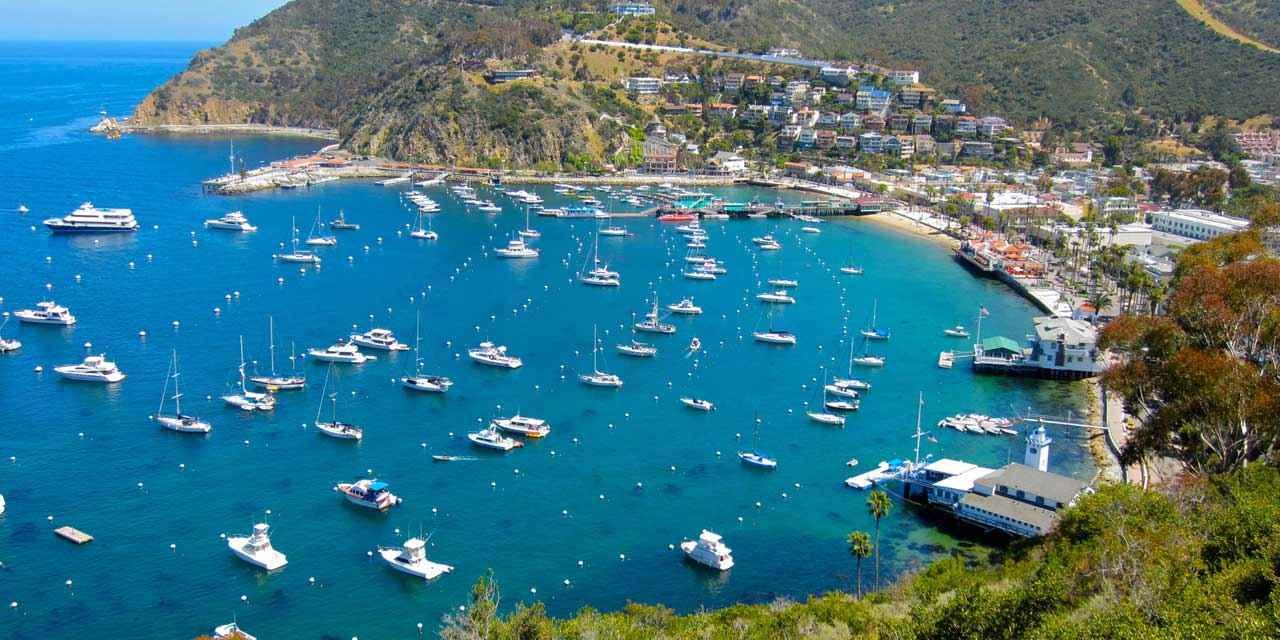 A turquoise bay filled with anchored boats beside a hillside coastal town