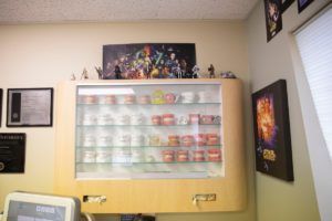Wall display case with colorful collectible figures on shelves in a beige room, with framed art on the walls.