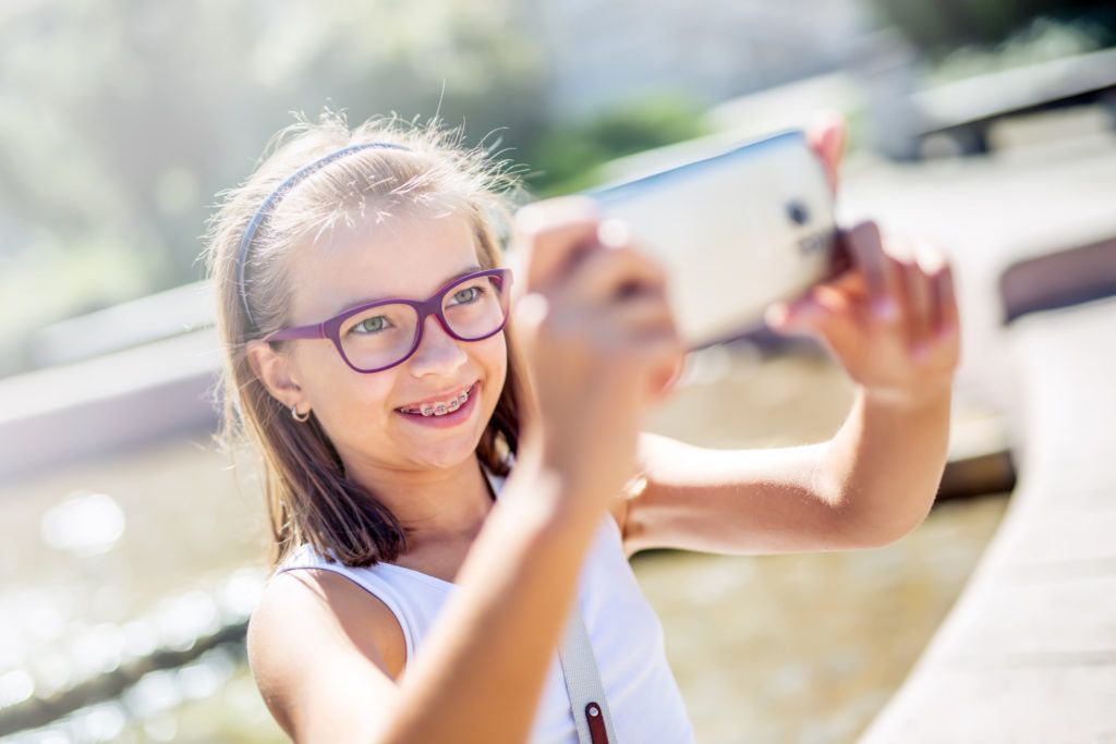 Smiling person with pink glasses taking a selfie outdoors near water