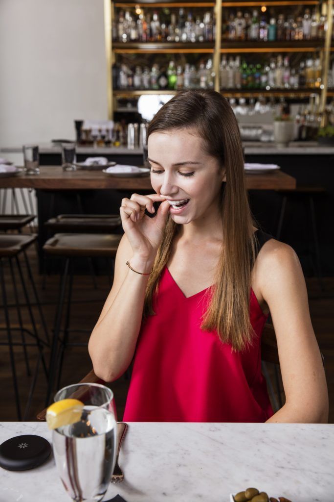 Woman in a red top looking at a smartphone at a café table with a glass of water and lemon.