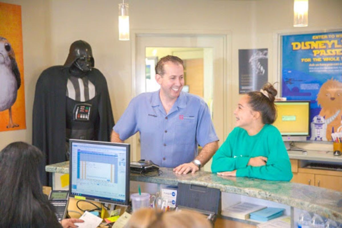 Two people chatting at a museum counter beside Darth Vader and Disney posters