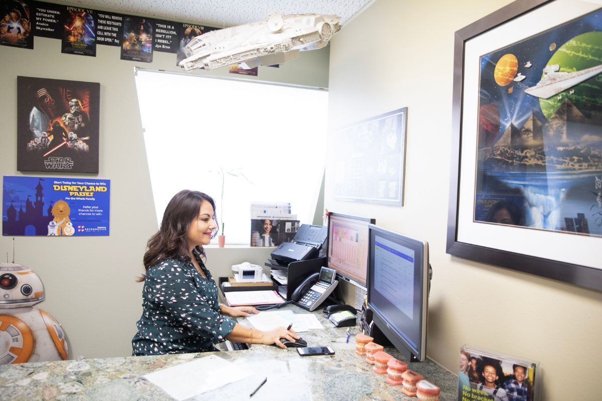 Woman working at a computer in a cluttered office, with posters on the walls and a desk full of papers.