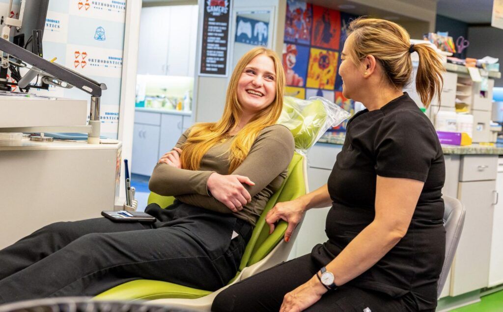 Two women talking in a bright office, seated in green chairs and smiling at each other.