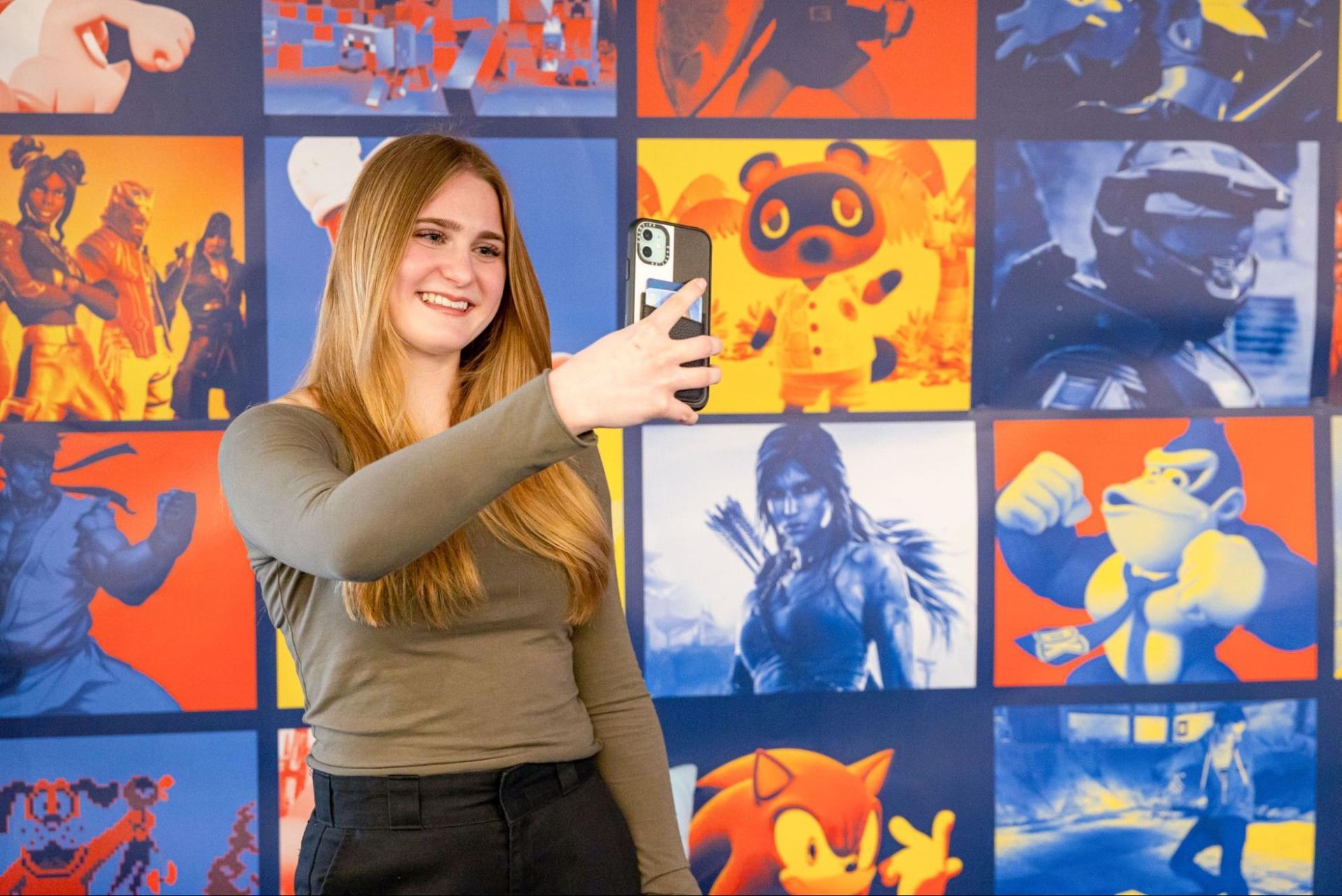 Woman smiling and holding a phone in front of a colorful wall of pop art posters