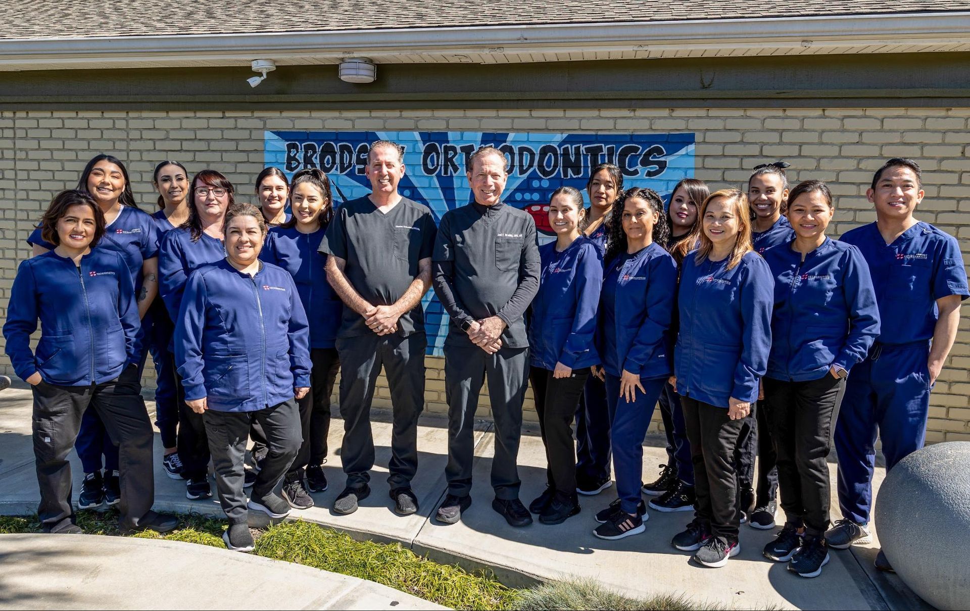 Group of people in blue shirts standing outside a building in front of a Brothers and Daughters sign
