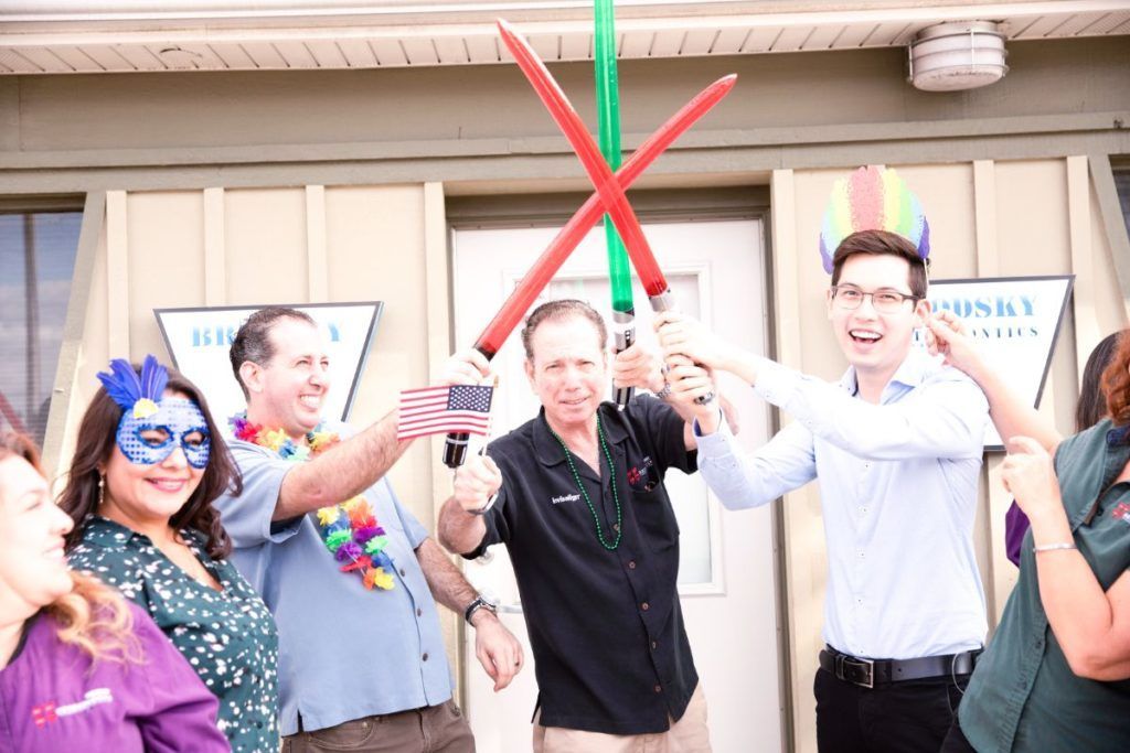 People cutting a red ribbon with large green scissors at a storefront opening