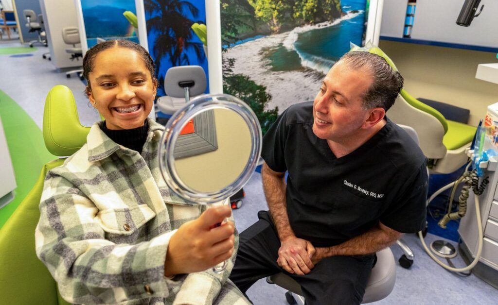 Woman smiling and holding a mirror while seated man looks on in a bright dental clinic